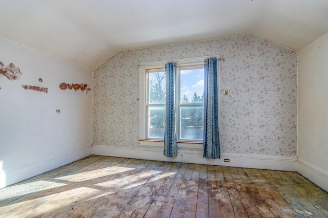 empty room featuring wallpapered walls, lofted ceiling, and wood-type flooring