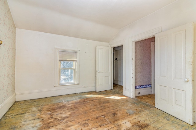 unfurnished bedroom with vaulted ceiling, wallpapered walls, and wood-type flooring