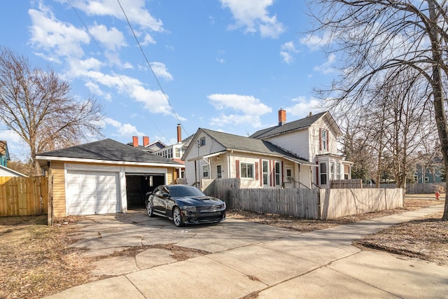 view of property exterior with an outbuilding, an attached garage, a chimney, concrete driveway, and a fenced front yard