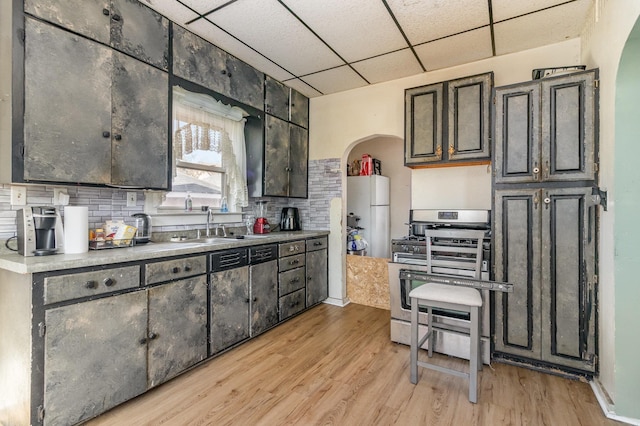 kitchen with stainless steel gas stove, light wood-style flooring, a sink, backsplash, and a paneled ceiling