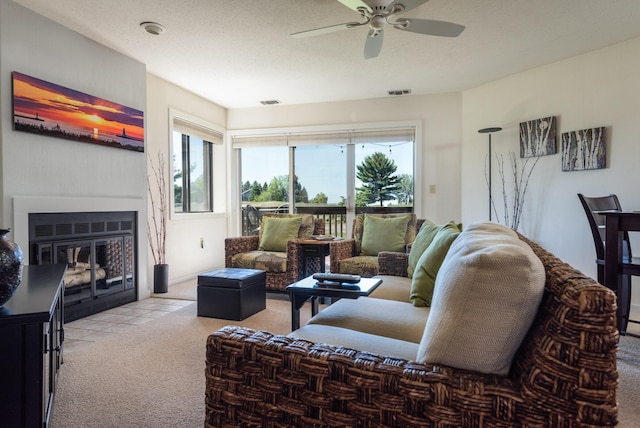 carpeted living area with visible vents, a fireplace with flush hearth, a textured ceiling, and a ceiling fan