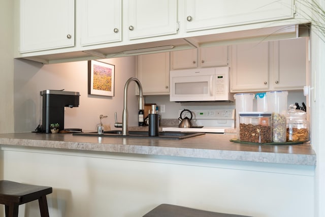 kitchen with white microwave, a sink, stove, white cabinets, and a kitchen bar