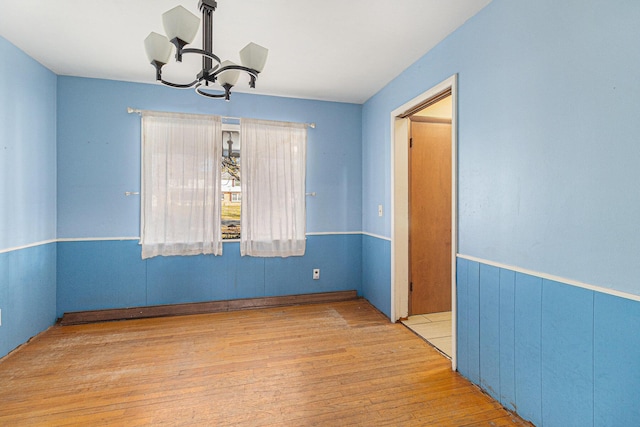 unfurnished room featuring hardwood / wood-style floors, a wainscoted wall, and a chandelier