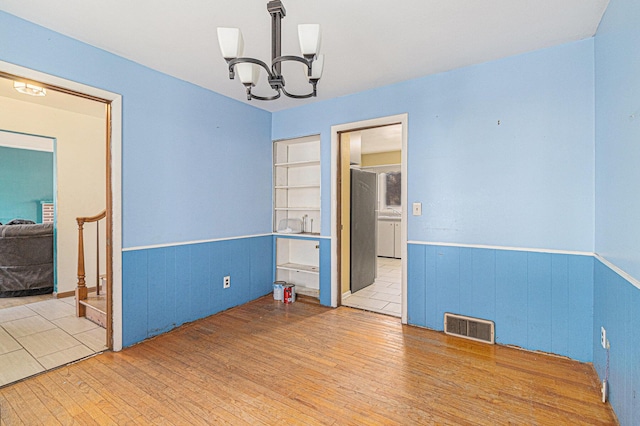 spare room featuring a chandelier, visible vents, wood-type flooring, and a wainscoted wall