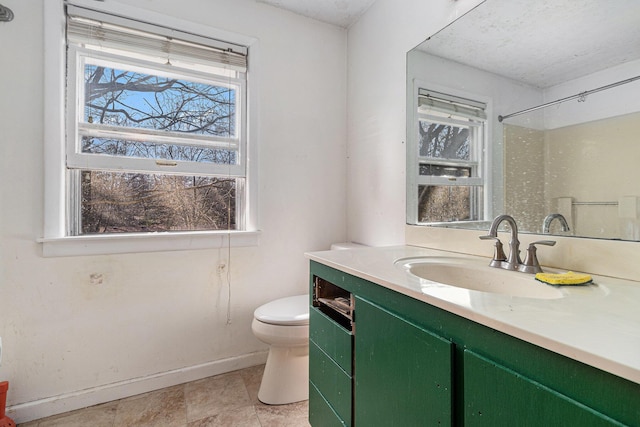 bathroom with toilet, plenty of natural light, vanity, and baseboards