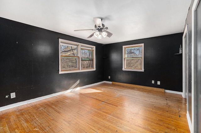 spare room featuring a ceiling fan, baseboards, wood-type flooring, and a healthy amount of sunlight