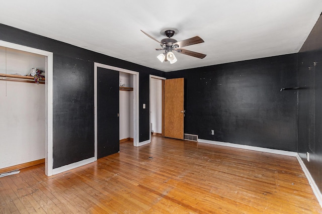 unfurnished bedroom featuring baseboards, visible vents, light wood-style flooring, ceiling fan, and two closets