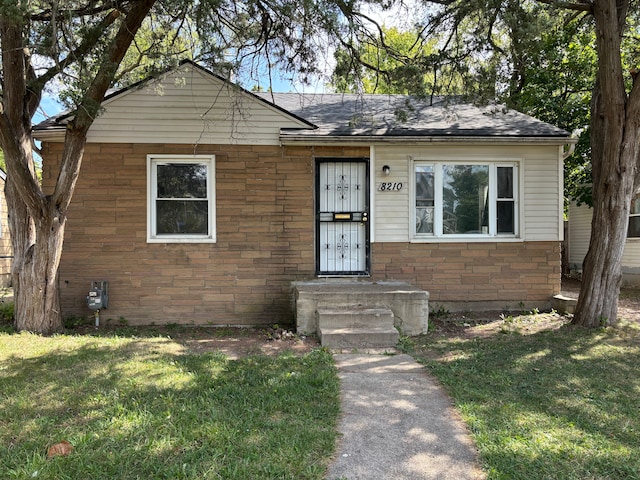 bungalow-style house with stone siding, roof with shingles, and a front yard