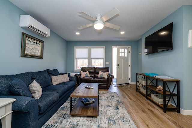 living area featuring baseboards, a ceiling fan, a wall unit AC, and wood finished floors