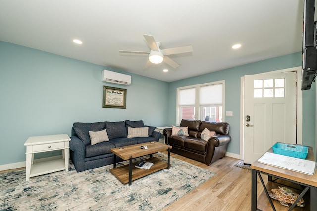 living room featuring a wall unit AC, baseboards, recessed lighting, ceiling fan, and light wood-type flooring