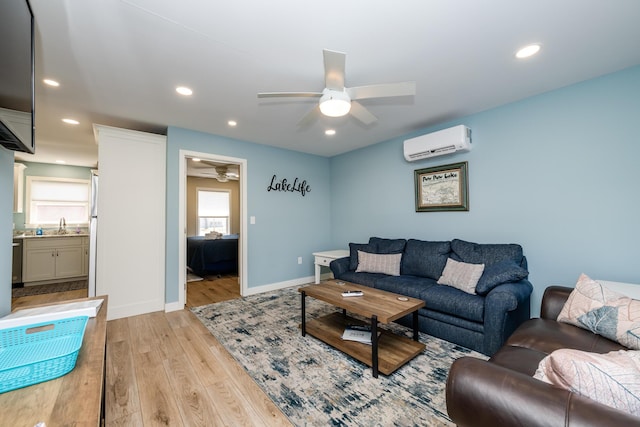 living area with a wall mounted air conditioner, recessed lighting, light wood-style floors, baseboards, and ceiling fan