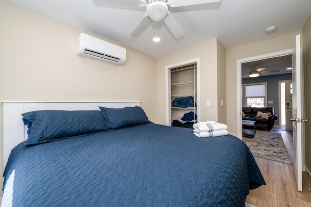 bedroom with a wall mounted air conditioner, light wood-type flooring, and a ceiling fan