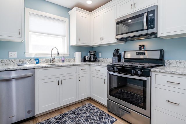 kitchen featuring light stone countertops, light wood finished floors, a sink, white cabinets, and appliances with stainless steel finishes