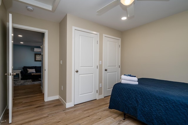 bedroom featuring a wall mounted air conditioner, recessed lighting, light wood finished floors, baseboards, and ceiling fan