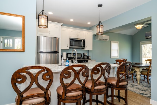 kitchen with light stone counters, a wall mounted AC, stainless steel appliances, white cabinetry, and a kitchen breakfast bar