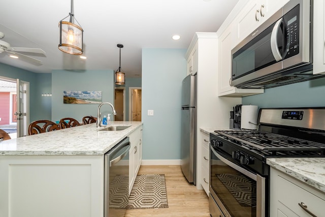 kitchen featuring appliances with stainless steel finishes, light wood-style floors, white cabinetry, a ceiling fan, and a sink