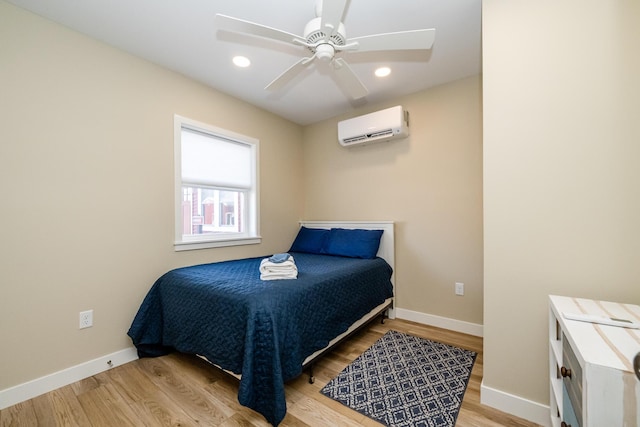 bedroom featuring wood finished floors, baseboards, and a wall mounted air conditioner