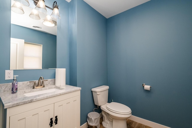 half bath featuring visible vents, toilet, wood finished floors, baseboards, and vanity