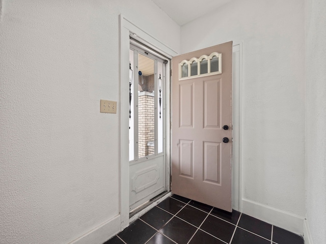 doorway to outside featuring dark tile patterned floors, a textured wall, and baseboards