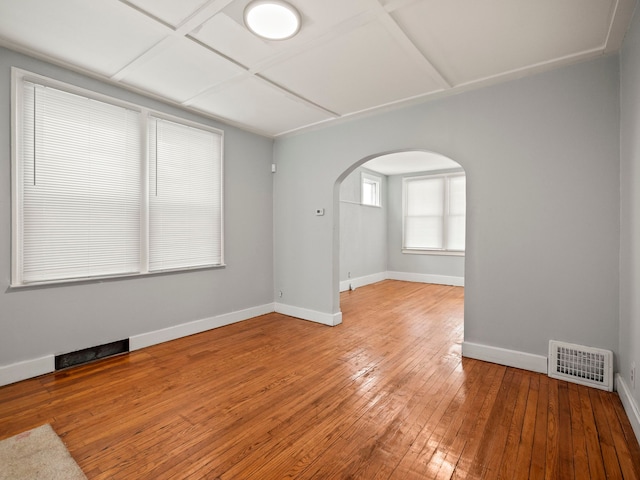 unfurnished room with arched walkways, visible vents, wood-type flooring, and baseboards