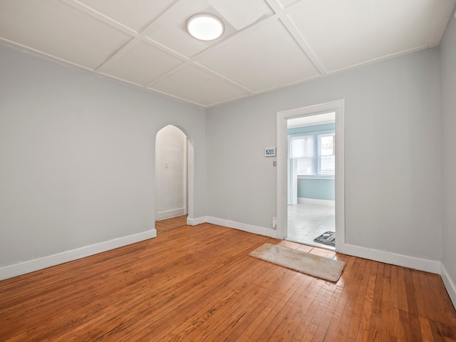 empty room featuring hardwood / wood-style flooring, baseboards, arched walkways, and coffered ceiling