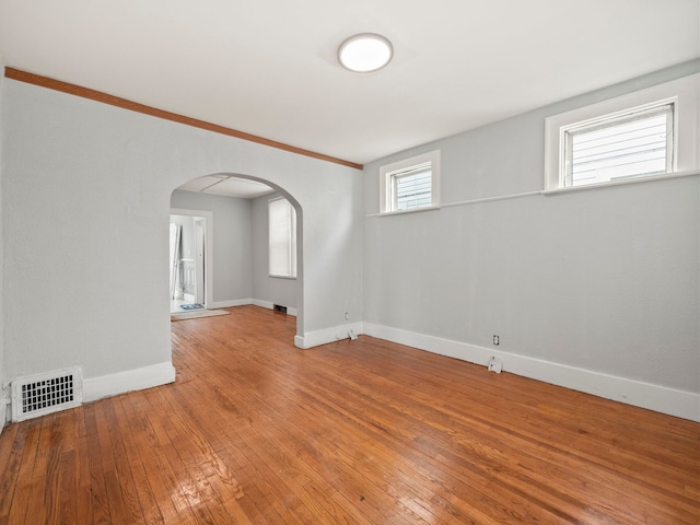 empty room featuring arched walkways, visible vents, baseboards, and wood-type flooring