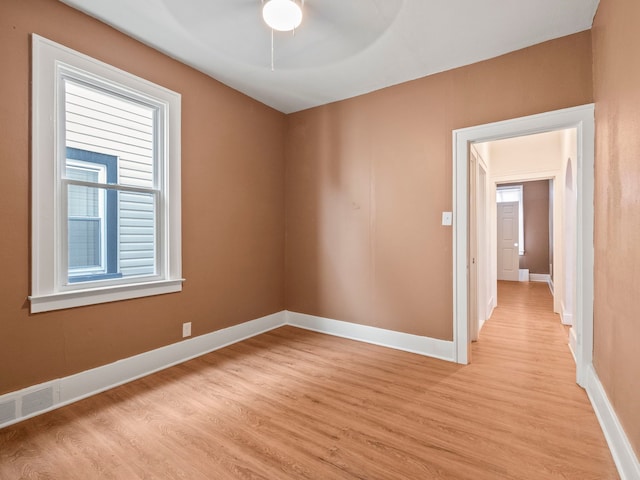 spare room featuring light wood finished floors, visible vents, a ceiling fan, and baseboards