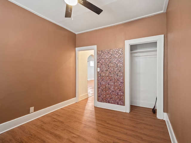 unfurnished bedroom with arched walkways, wood finished floors, baseboards, and ceiling fan