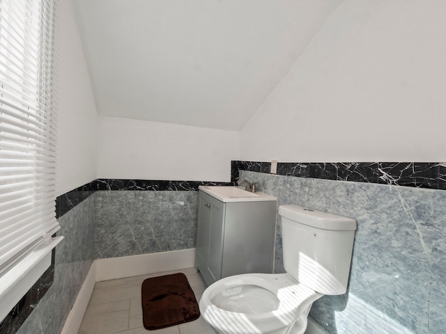 half bath with vanity, lofted ceiling, tile walls, toilet, and tile patterned floors