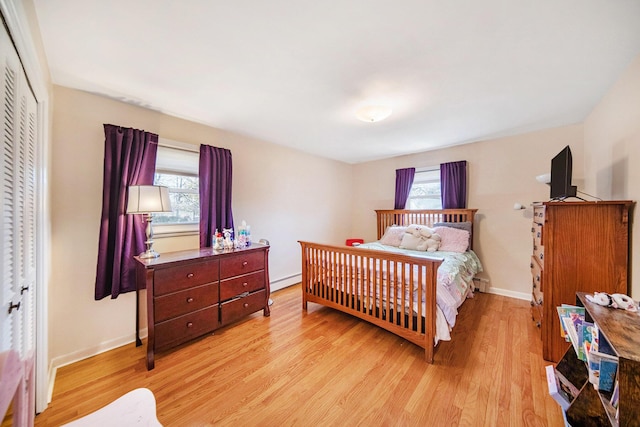 bedroom featuring a closet, baseboard heating, light wood-type flooring, and baseboards