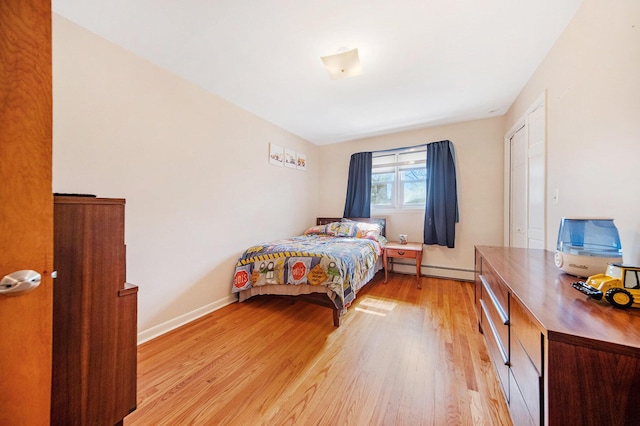 bedroom with a baseboard heating unit, baseboards, and light wood-style floors