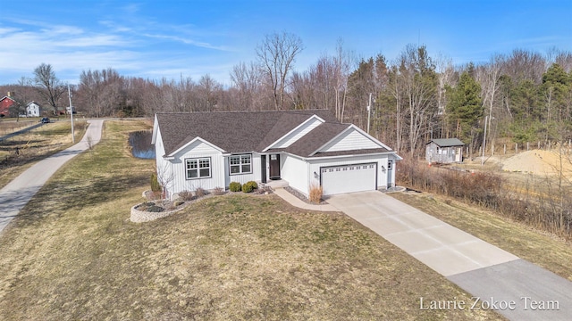 view of front facade featuring a forest view, a garage, concrete driveway, and a front yard