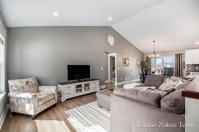 living area with baseboards, visible vents, lofted ceiling, light wood-style flooring, and a notable chandelier