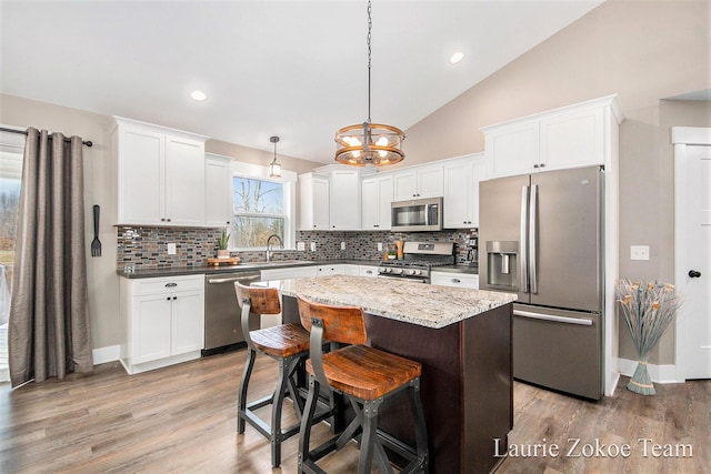 kitchen featuring a kitchen island, a chandelier, stainless steel appliances, wood finished floors, and white cabinetry