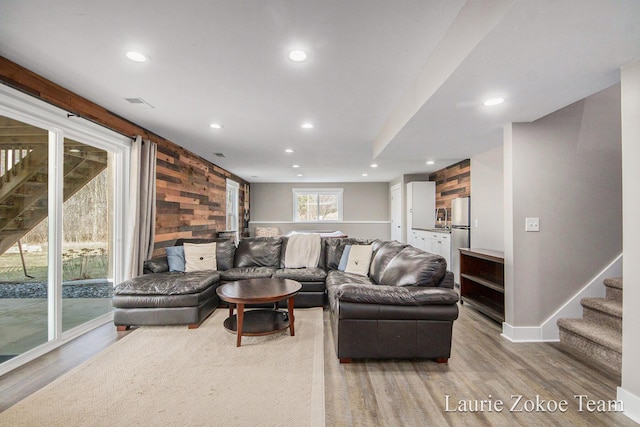 living room with wooden walls, recessed lighting, stairs, and light wood-style floors