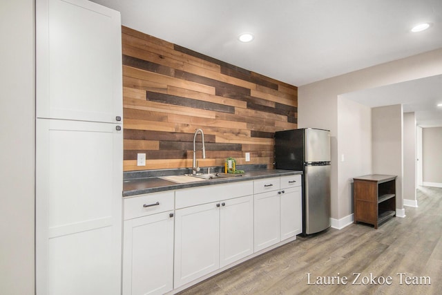 kitchen with dark countertops, wooden walls, light wood-style flooring, freestanding refrigerator, and a sink