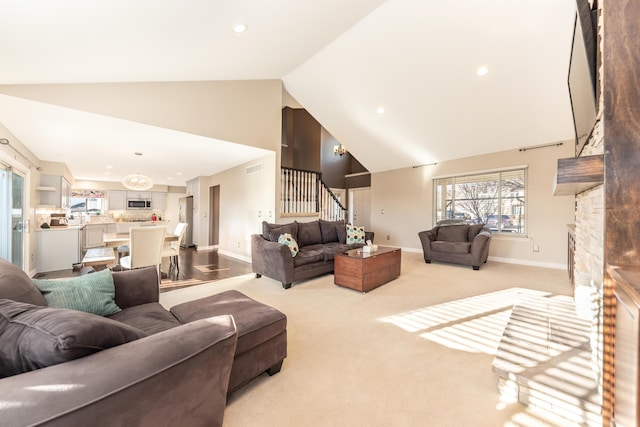 living room with baseboards, light colored carpet, stairs, a fireplace, and high vaulted ceiling