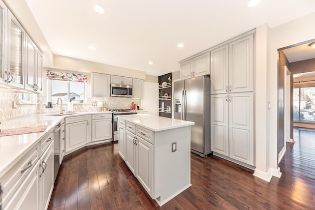 kitchen featuring a kitchen island, a sink, light countertops, appliances with stainless steel finishes, and tasteful backsplash