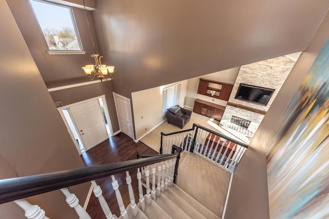 stairs with wood finished floors, baseboards, high vaulted ceiling, a stone fireplace, and a chandelier
