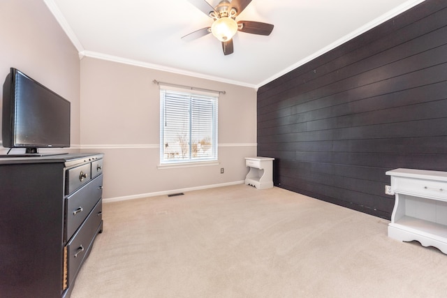 bedroom with wood walls, crown molding, baseboards, light colored carpet, and ceiling fan