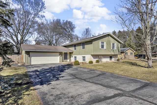 split level home with aphalt driveway, an attached garage, fence, and a front yard