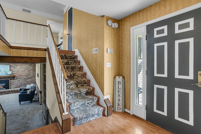 entryway featuring stairs, a brick fireplace, and wood finished floors