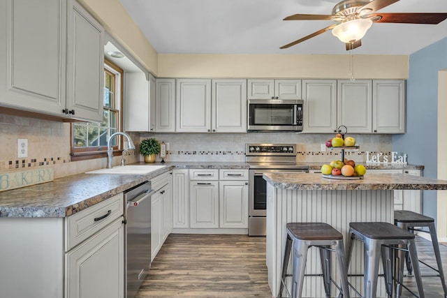 kitchen featuring backsplash, ceiling fan, appliances with stainless steel finishes, a kitchen breakfast bar, and a sink