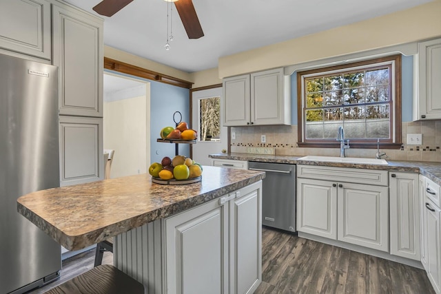 kitchen with a sink, a kitchen breakfast bar, dark wood-style floors, stainless steel appliances, and decorative backsplash