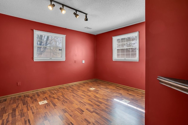 empty room featuring visible vents, track lighting, baseboards, wood finished floors, and a textured ceiling