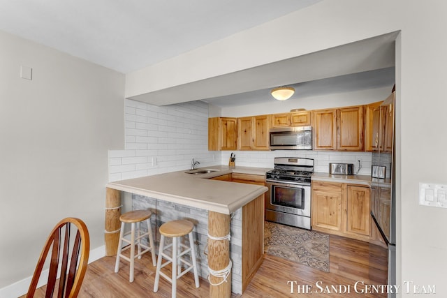 kitchen featuring a breakfast bar area, decorative backsplash, appliances with stainless steel finishes, a peninsula, and a sink