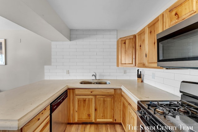 kitchen with a sink, tasteful backsplash, stainless steel appliances, light wood-style floors, and light countertops