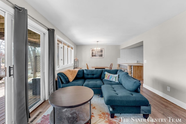 living room with a chandelier, visible vents, baseboards, and wood finished floors