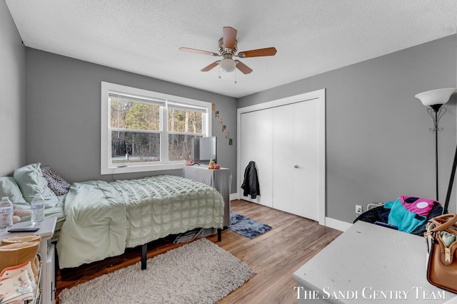 bedroom with a textured ceiling, wood finished floors, a closet, baseboards, and ceiling fan