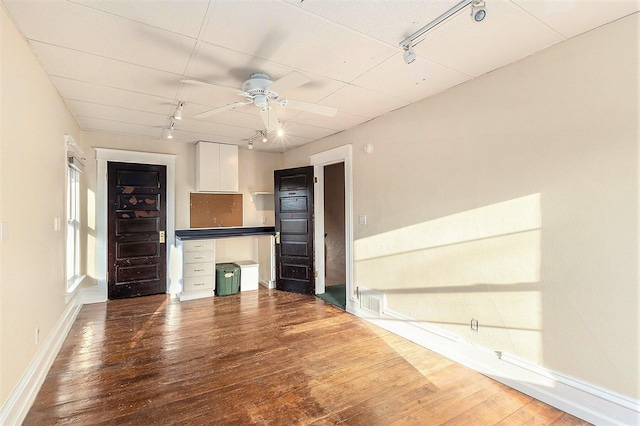 unfurnished living room with wood finished floors, a ceiling fan, baseboards, and track lighting